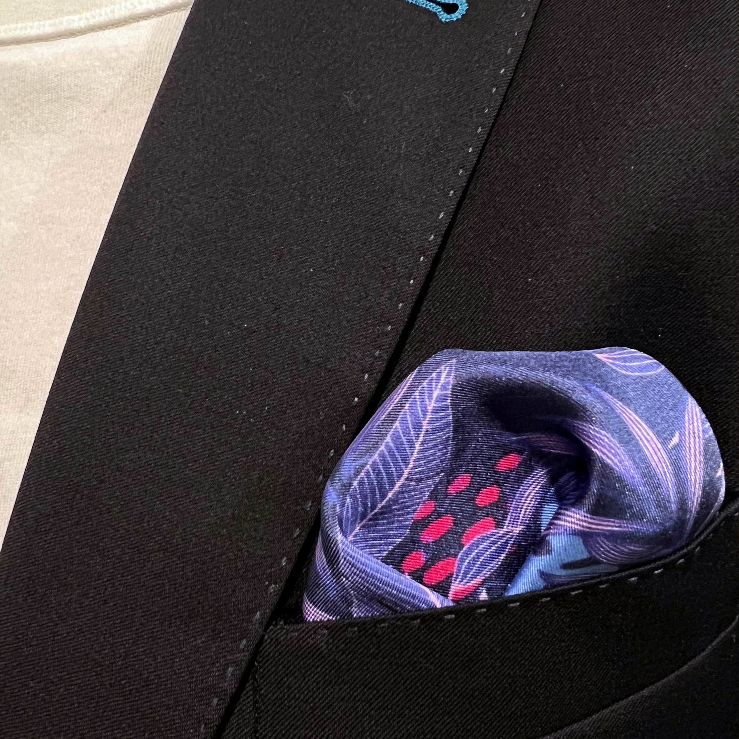 Silk square handkerchief with floral pattern on a purple-blue ground and placed in a jacket breast pocket.
