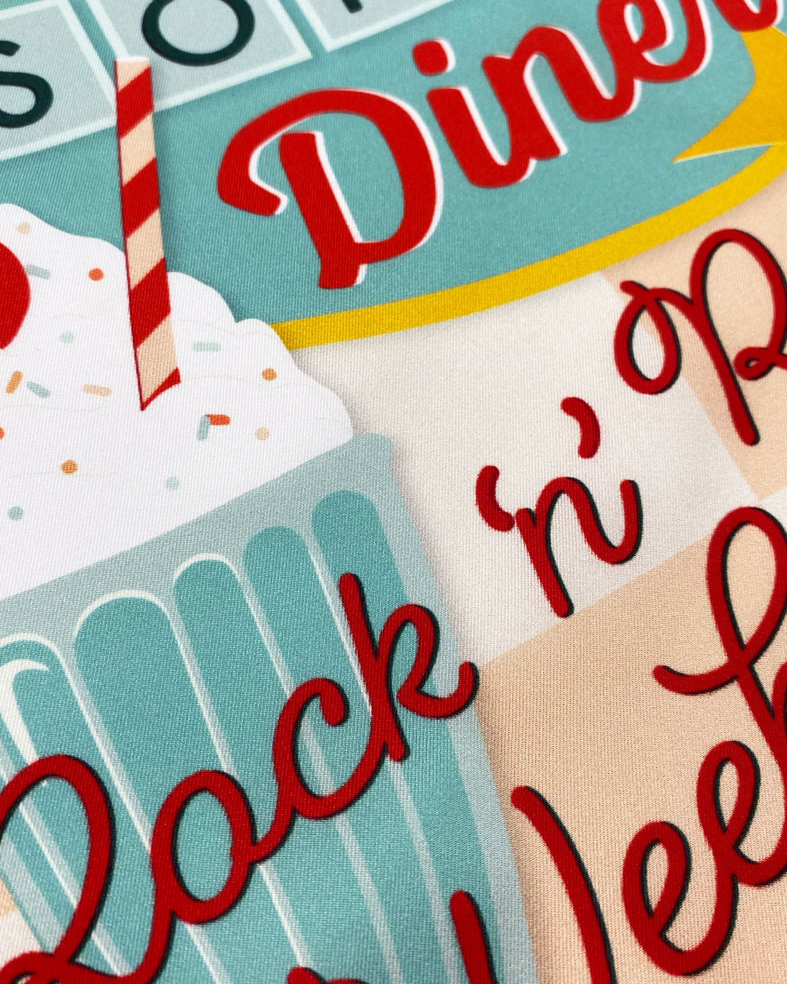 A ruffled close-up of the 'Milkshake' on chalk silk pocket square, presenting a closer look at a portion of the diner signage design.