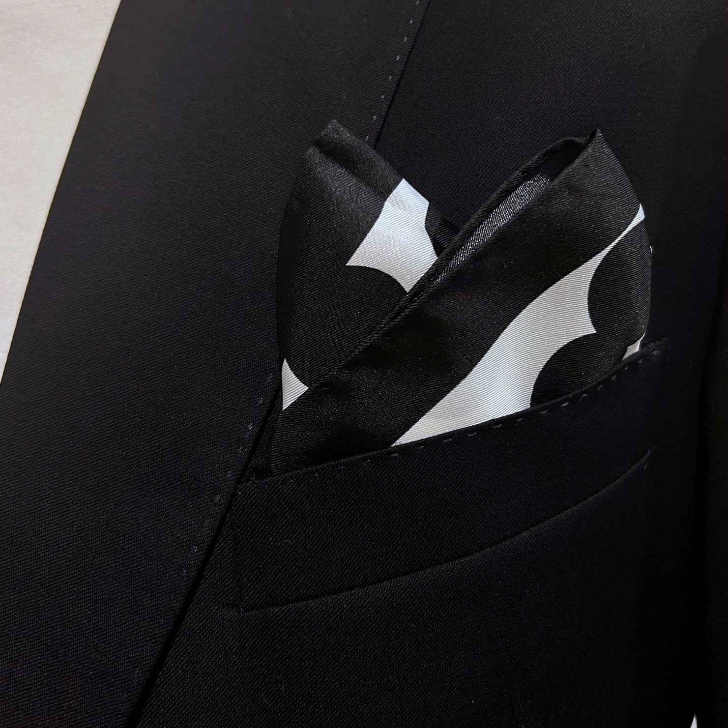 Close-up of black spotted 'Chaney' silk pocket square in breast pocket of dark suit jacket.