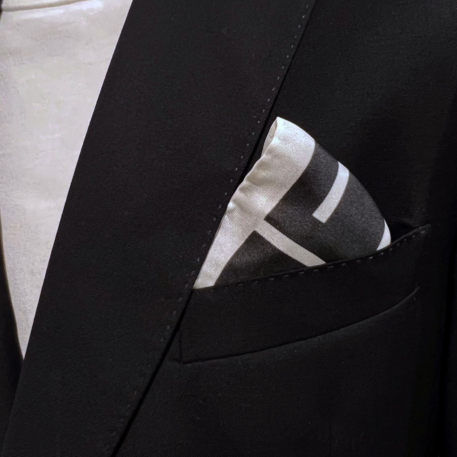 Close-up of striped 'Lloyd' silk pocket square in breast pocket of dark suit jacket.
