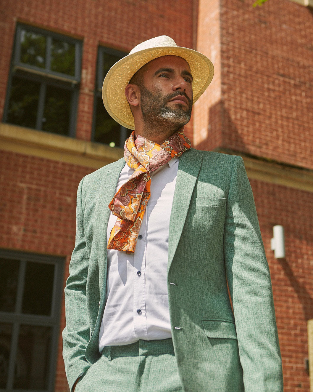 Outdoor top-half model shot wearing 'The Niagra' polyester, orange and pink floral scarf in a simple Parisian knot and paired with a mint-green casual suit.