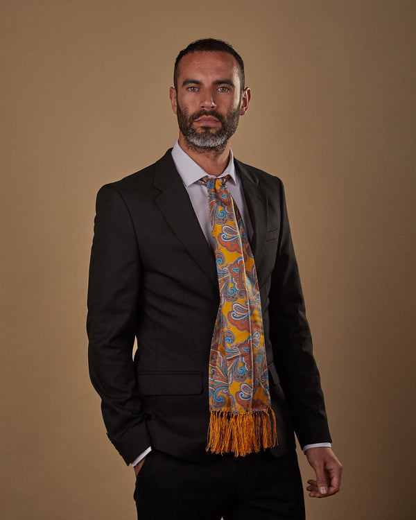 Three quarters front view of model wearing 'The Carnaby Aviator' gold silk scarf in a basic knot snugly round neck. Paired with white shirt and charcoal suit.
