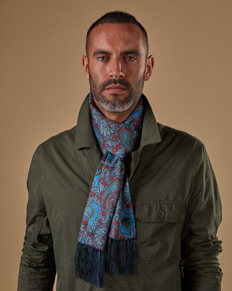 Head and shoulders view of model wearing blue and deep red paisley 'Dean Aviator' in a Parisian knot and paired with a dark green overshirt.