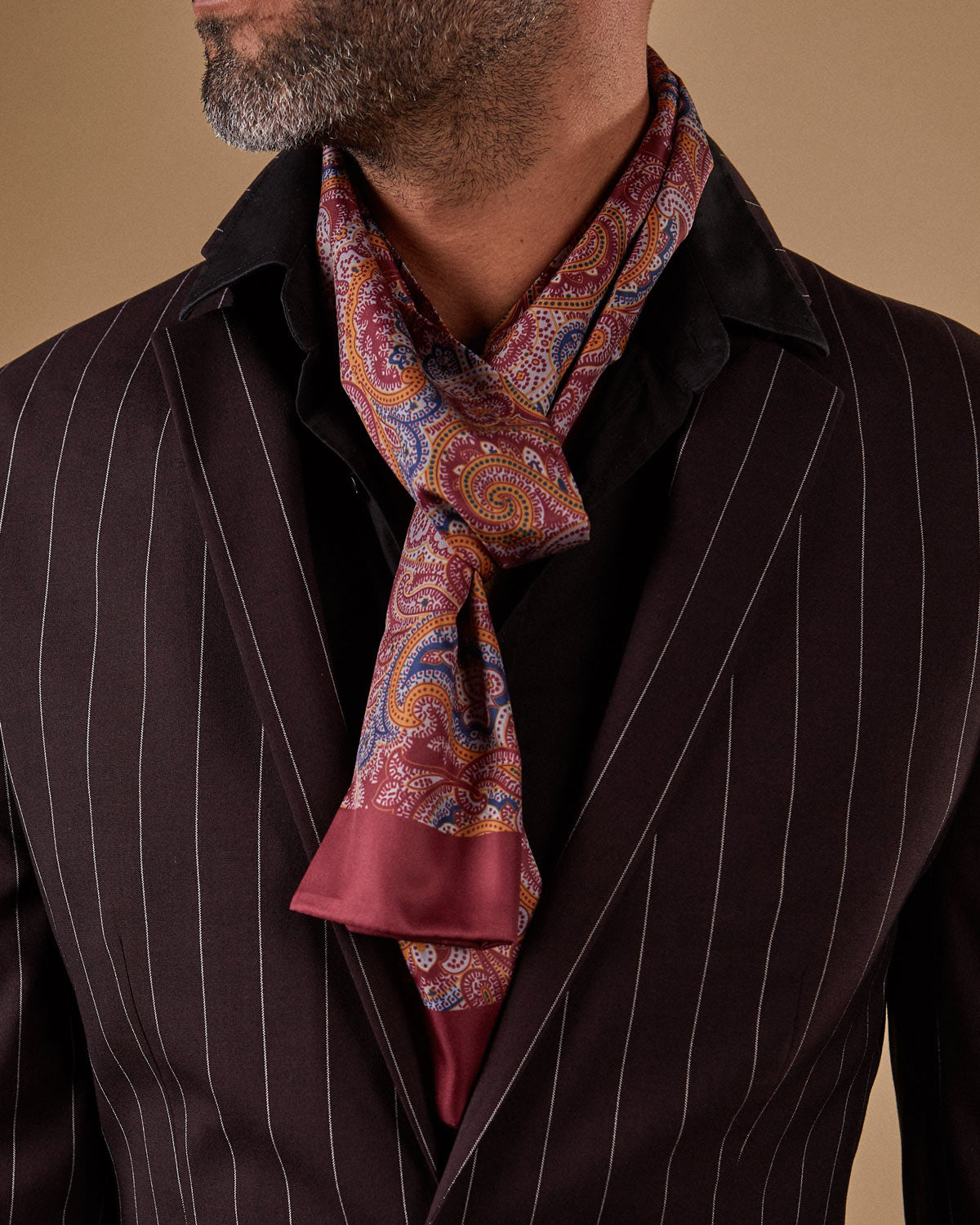Close-up shot of model wearing 'The Fanelli' paisley scarf in a loose knot and paired with dark, pinstriped jacket.