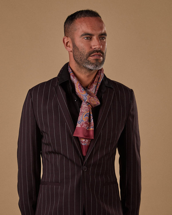 Model wearing 'The Fanelli' dark blue, gold and maroon paisley scarf in a loose knot and paired with dark, pinstriped jacket.