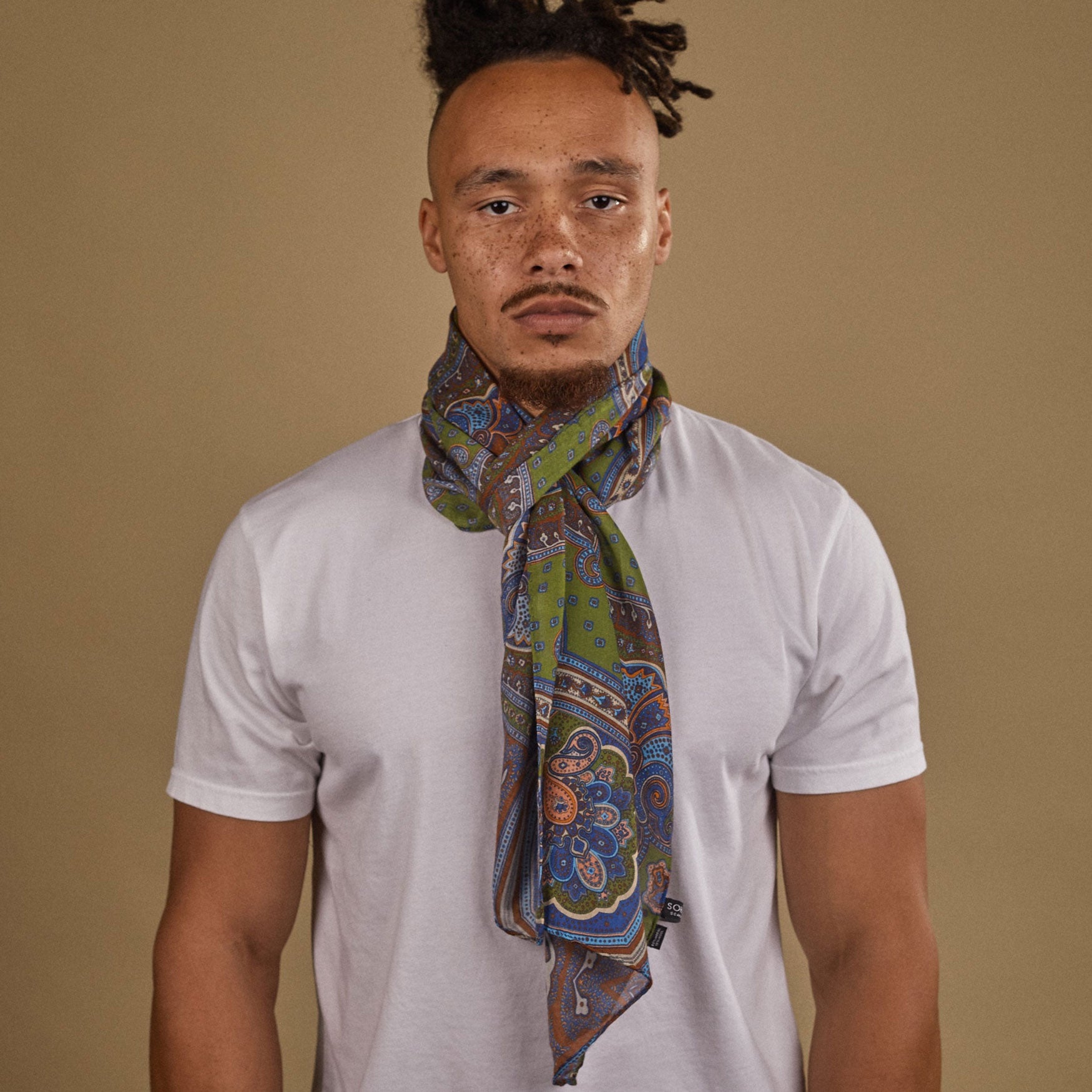 Close-up of model looking straight ahead wearing 'The Montreal' multicoloured extra-large paisley patterned wide bohemian scarf. Wrapped snugly around neck in a simple knot and paired with a white t-shirt.