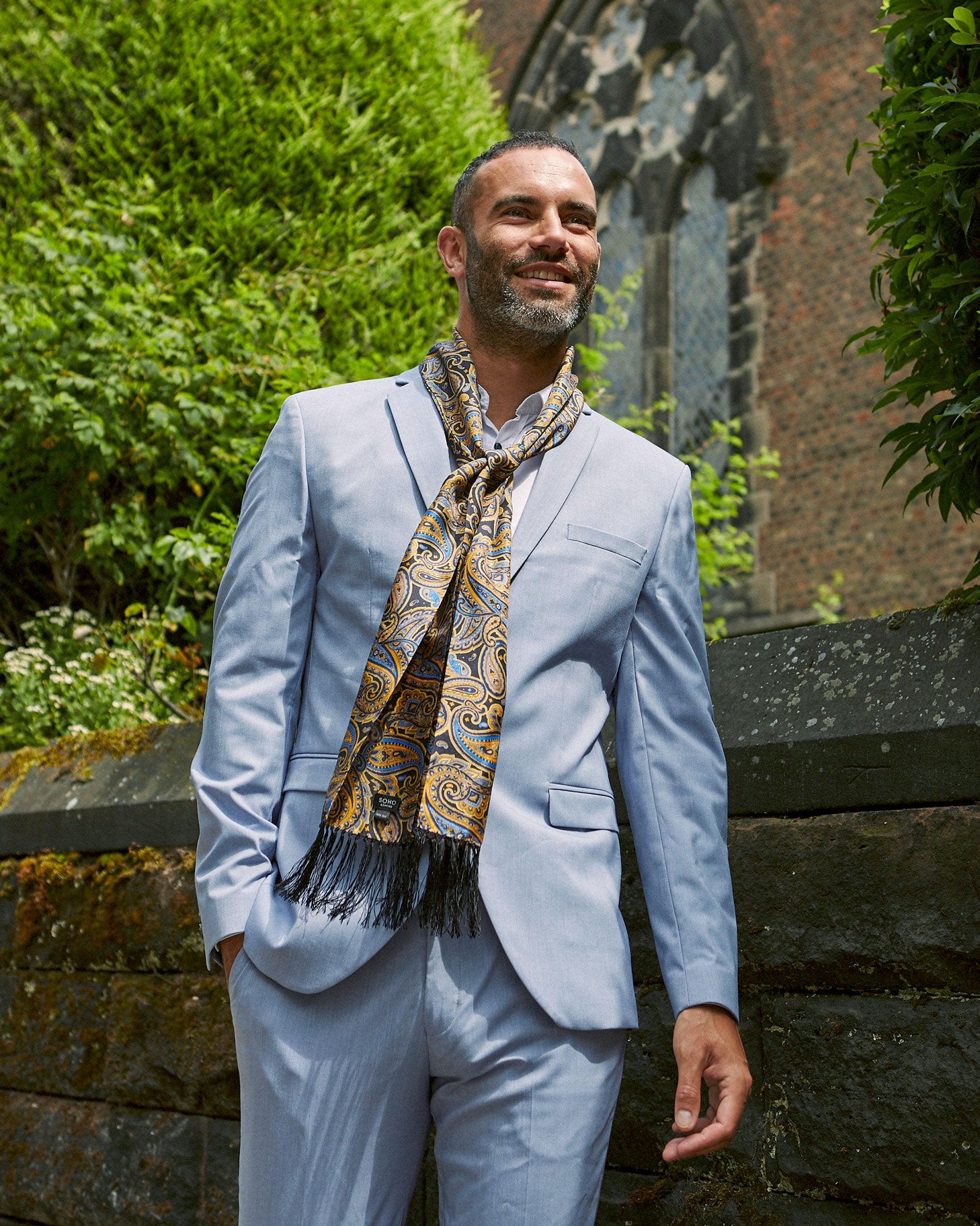 Outdoor shot wearing loosely tied 'The Ormond' aviator scarf paired with light blue-grey suit.