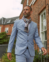 Outdoor shot modelling 'The Tremblant' multicoloured polyester scarf arranged in a simple Parisian knot. Paired with a pale blue casual suit.