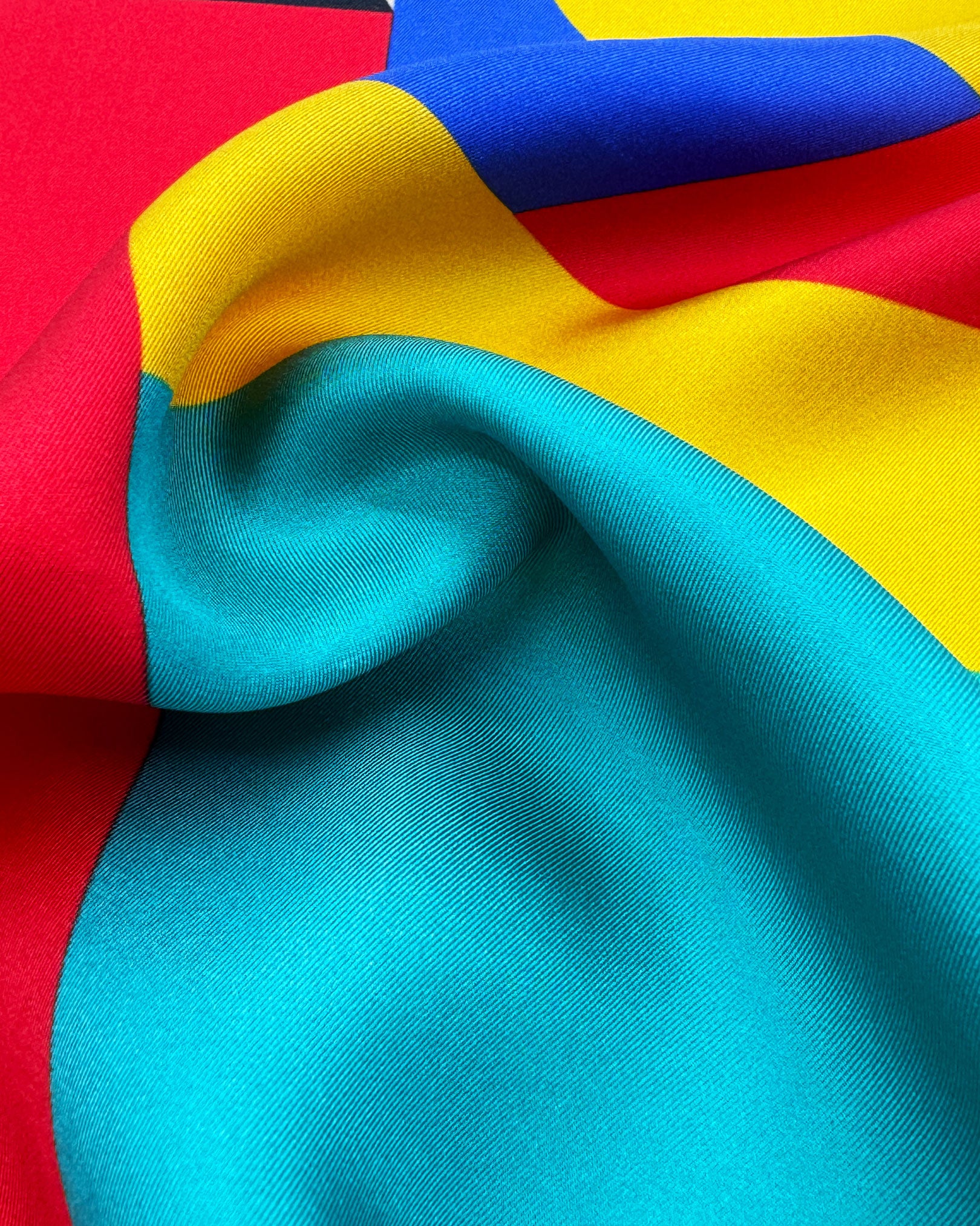 A ruffled close-up of the 'Munich' silk neckerchief, presenting a closer view of the Bauhaus-inspired, primary coloured patterns.