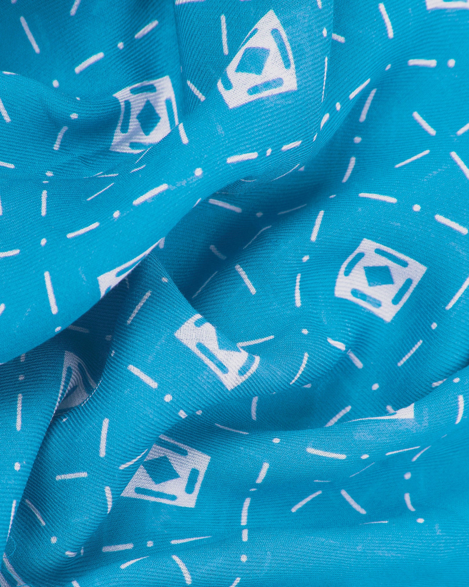 A ruffled close-up of the 'Diamonds in Pacific' modal and wool bandana from SOHO Scarves, highlighting the soft modal and wool blend fabric with repeating diamond frames, lozenges and crosshair motifs in contrasting Pacific blue tones.