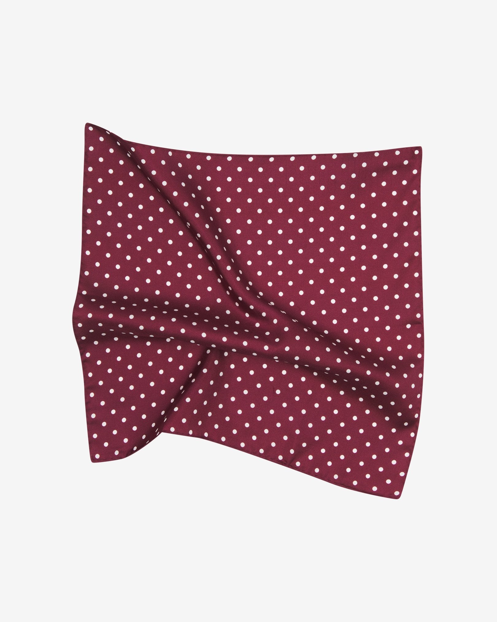 The 'Sapporo' silk pocket square pinched and twisted in the middle, showing polka dot pattern set on a deep red fabric background.
