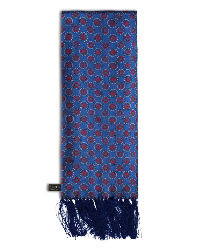 'The Bellevue Aviator' blue silk scarf with small circular and floral-inspired patterns in red and maroon, with white and dark grey highlights. Scarf arranged in a rectangular shape, clearly showing the dark-blue 3-inch fringe and the 'Soho Scarves' label on the left edge.