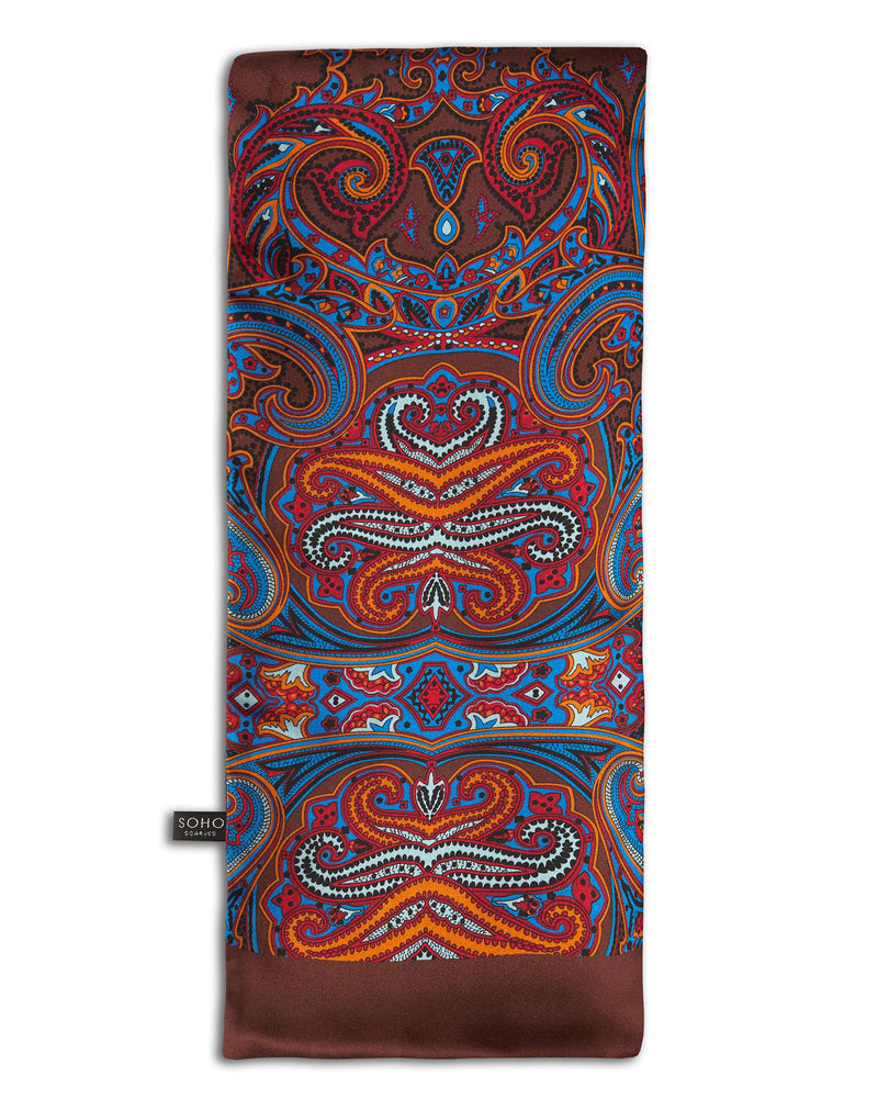 'The Fresco' brown, wool-backed scarf arranged in a rectangular shape, clearly showing the large, paisley-inspired patterns in mid-blue, black, orange, white and red, with the 'Soho Scarves' label on the left edge.