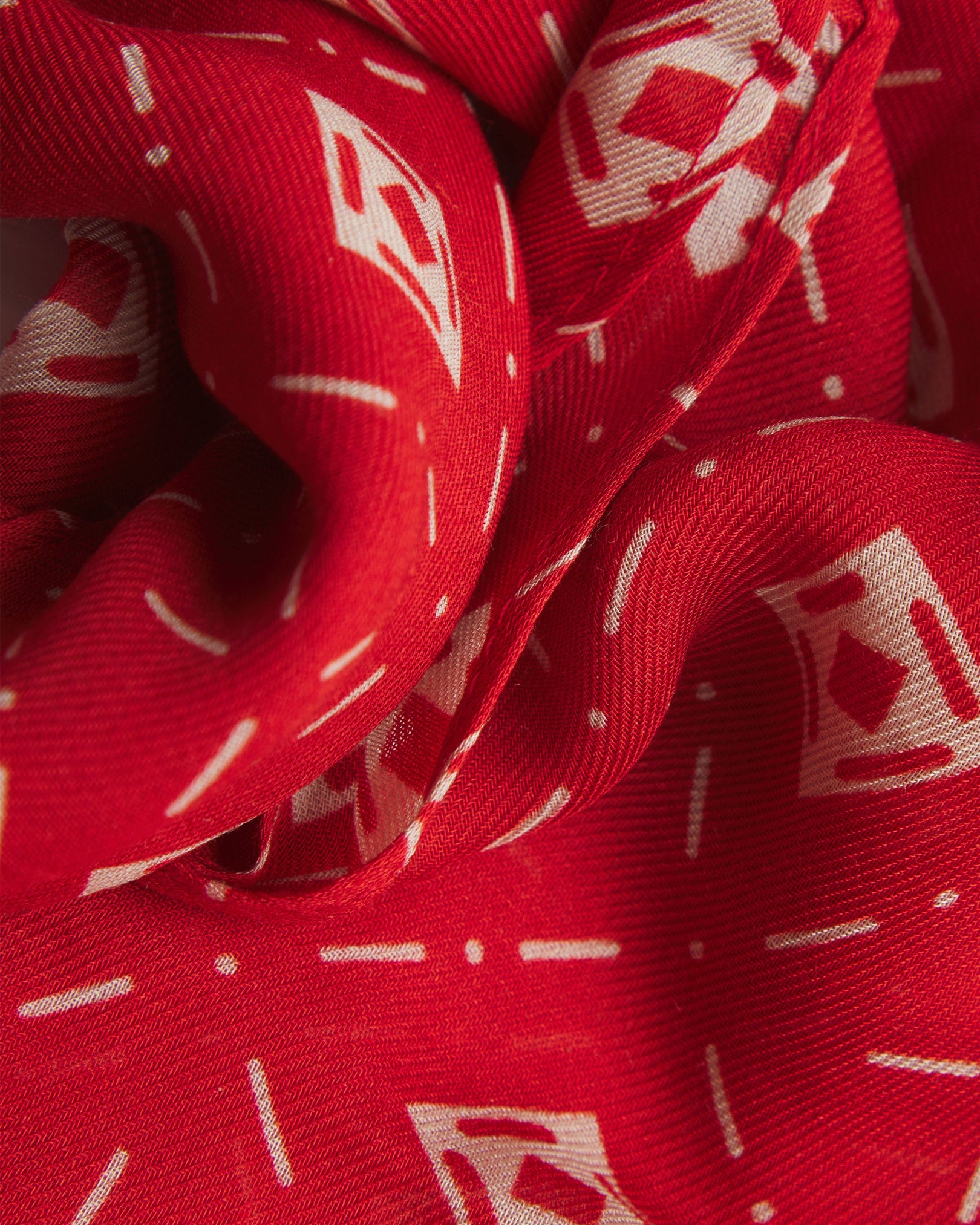 A ruffled close-up of the 'Diamonds' red bohemian wide scarf, showing the soft modal and wool blend fabric with an ordered diamond mosaic of white lozenges and crosshair motifs on a bright red background.