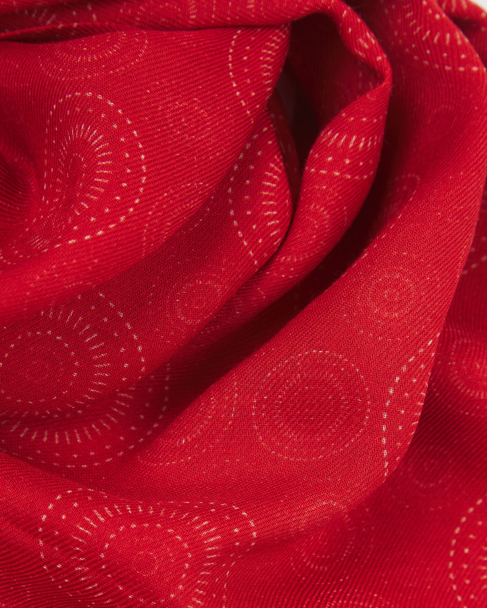 A ruffled close-up of the 'Circles' red bohemian wide scarf, showing the soft modal and wool blend fabric with concentric Op art-inspired disc motifs in white on a bright red background.