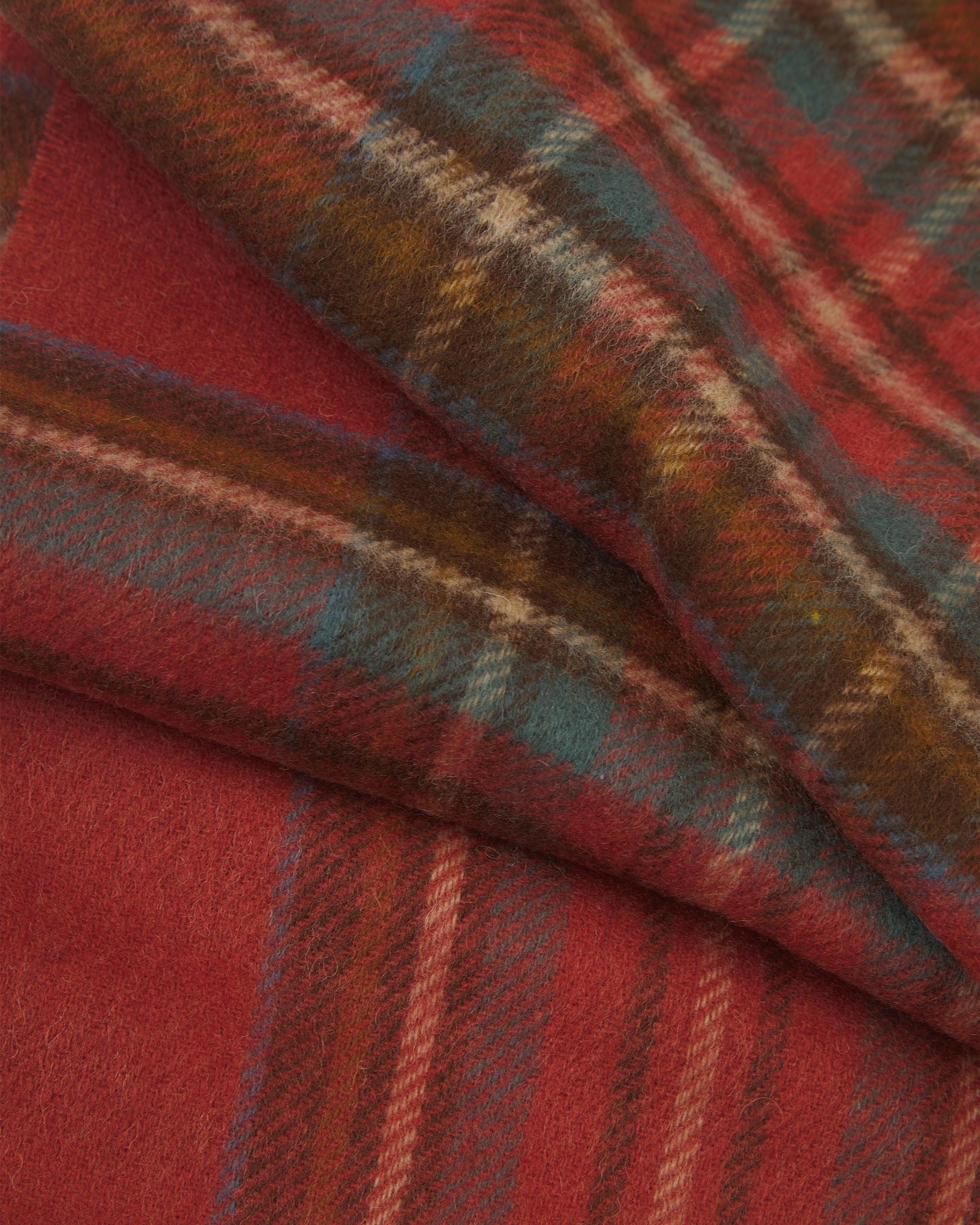 Ruffled close-up view of the UK-made, pure Merino wool 'Highlands' tartan in rust scarf, presenting a closer view of the light blue, cream, and brown interlocking tartan pattern.