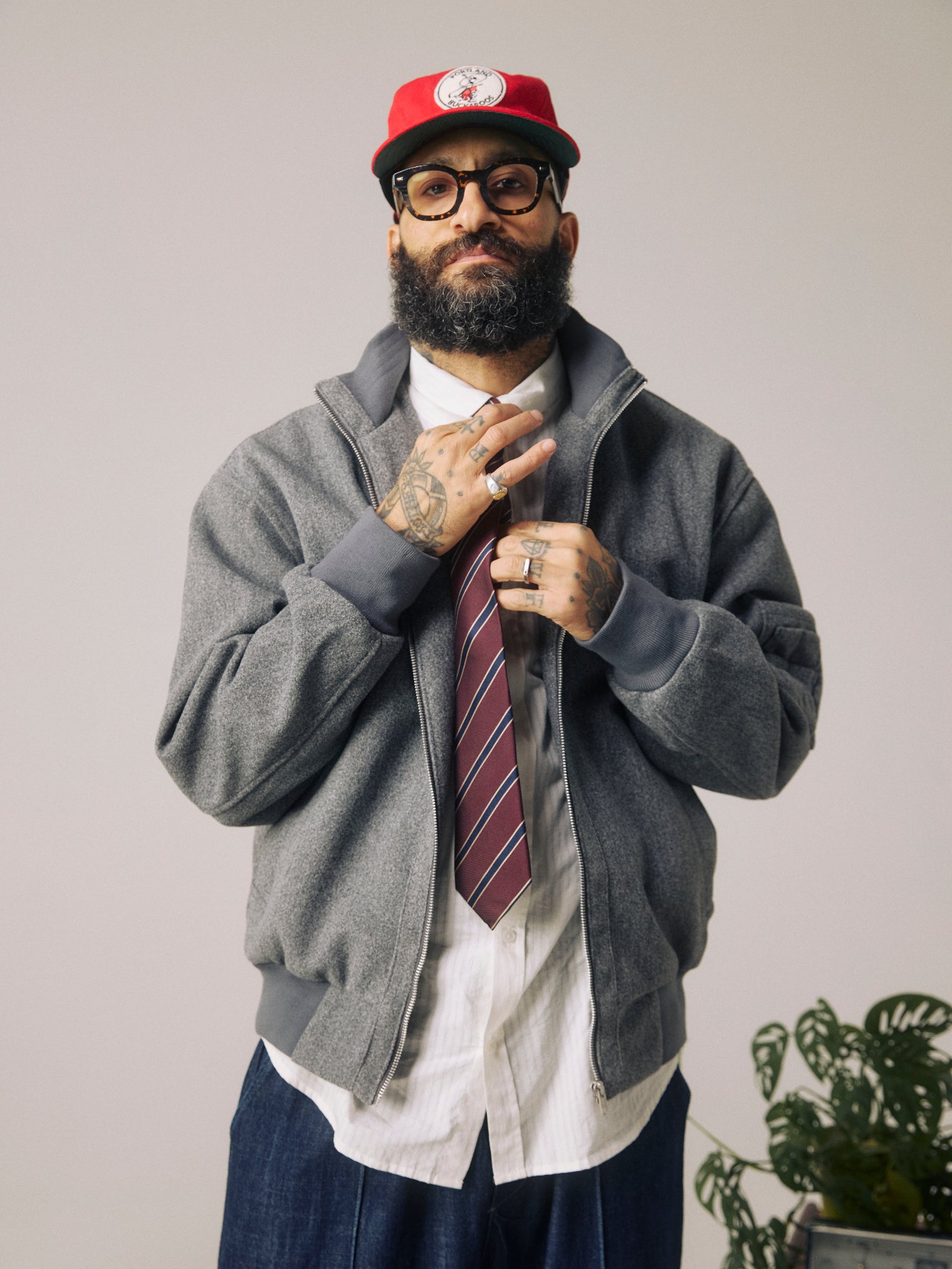 Front view of man adjusting the 'Sanders Mahogany Haze' silk neck tie. Paired with wool grey jacket and red cap.