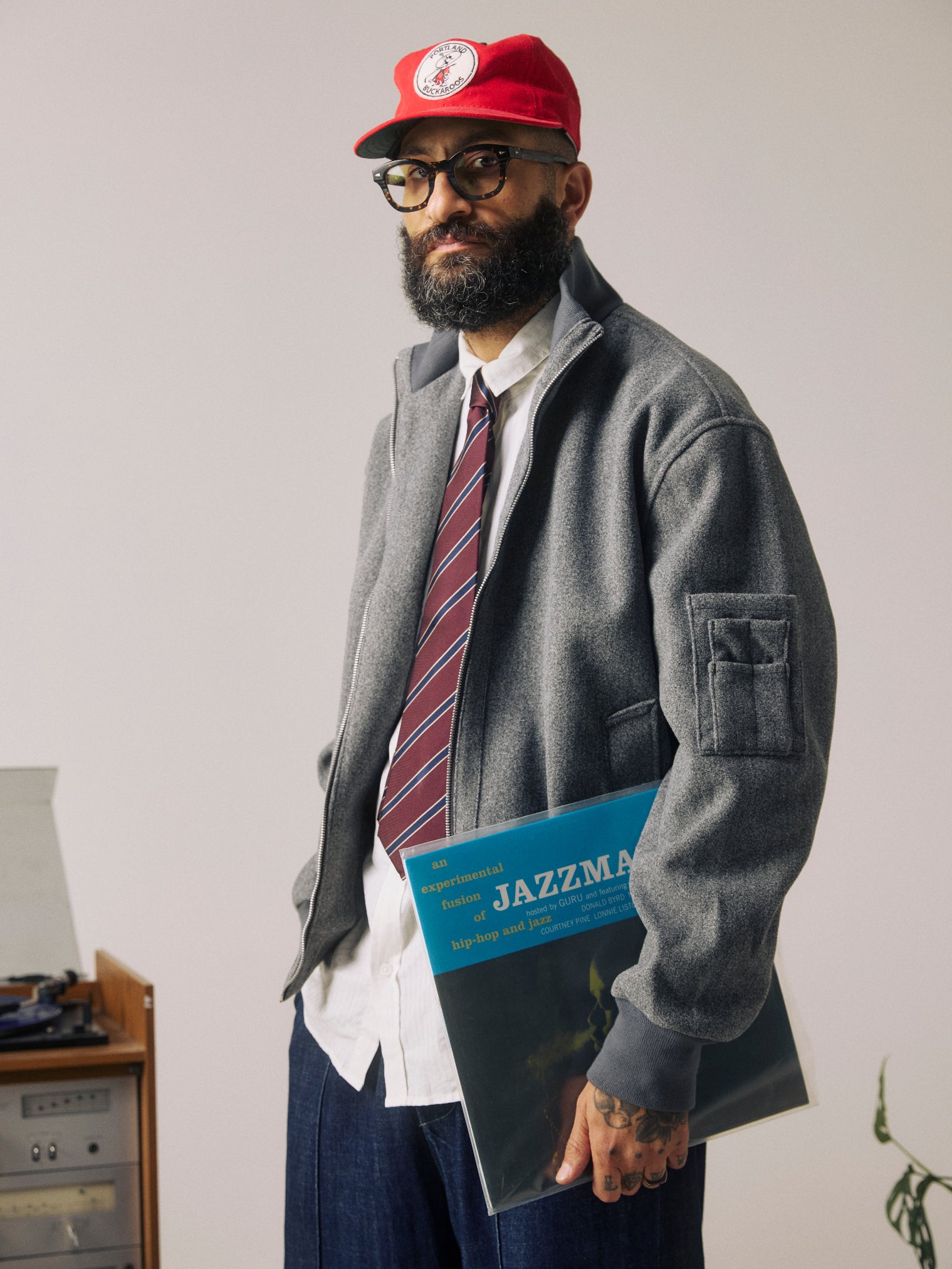 Side view of man wearing the 'Sanders Mahogany Haze' silk neck tie with narrow diagonal gold and navy stripes on a maroon ground. Paired with wool grey jacket.