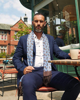 Model seated at a cafe with 'The Myers' blue and brown paisley aviator scarf casually draped around neck and paired with navy suit.