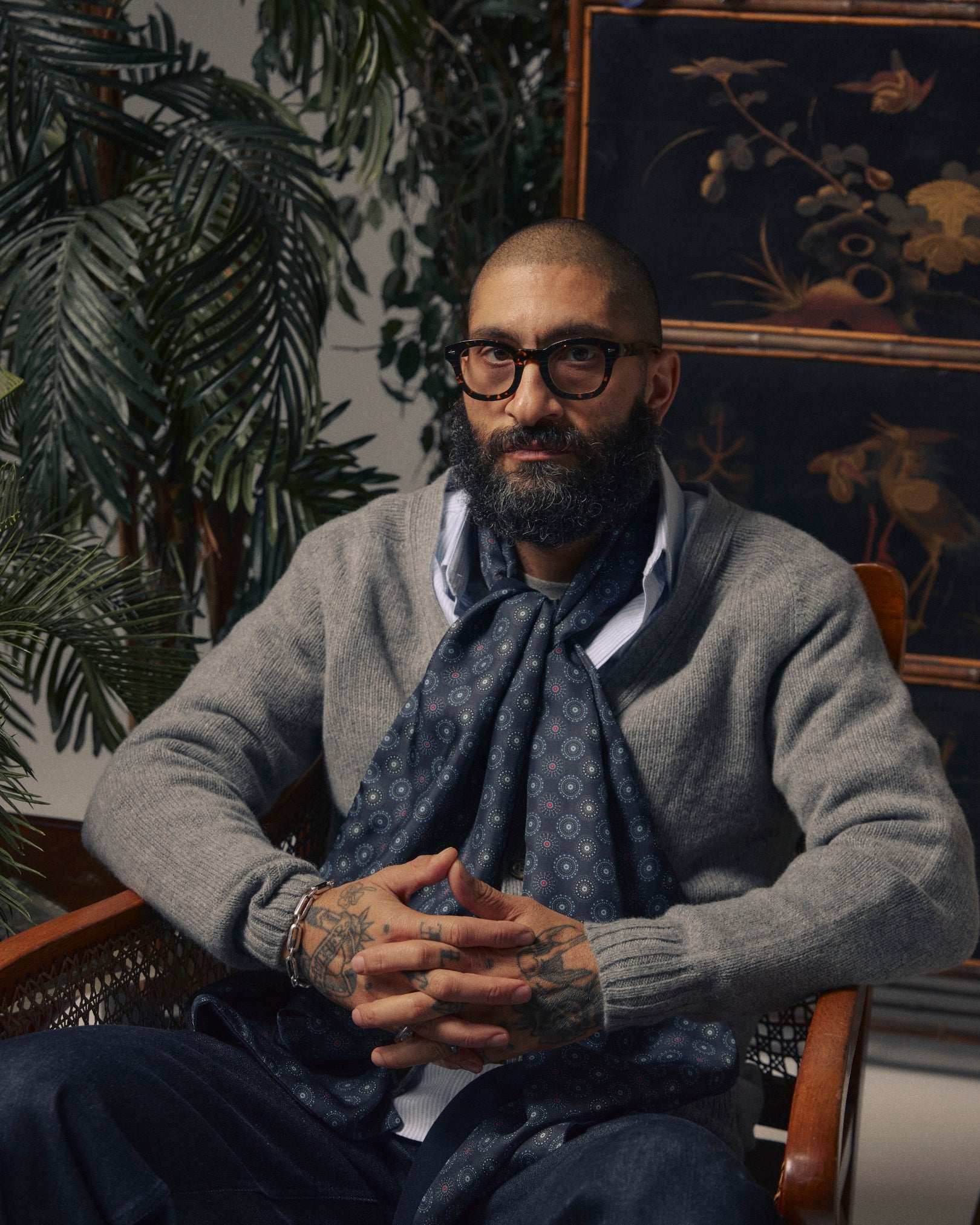 Man seated wearing the Seattle 'Gardenia' wool-backed silk dress scarf. Sitting in a room with plants and decorative wall art.