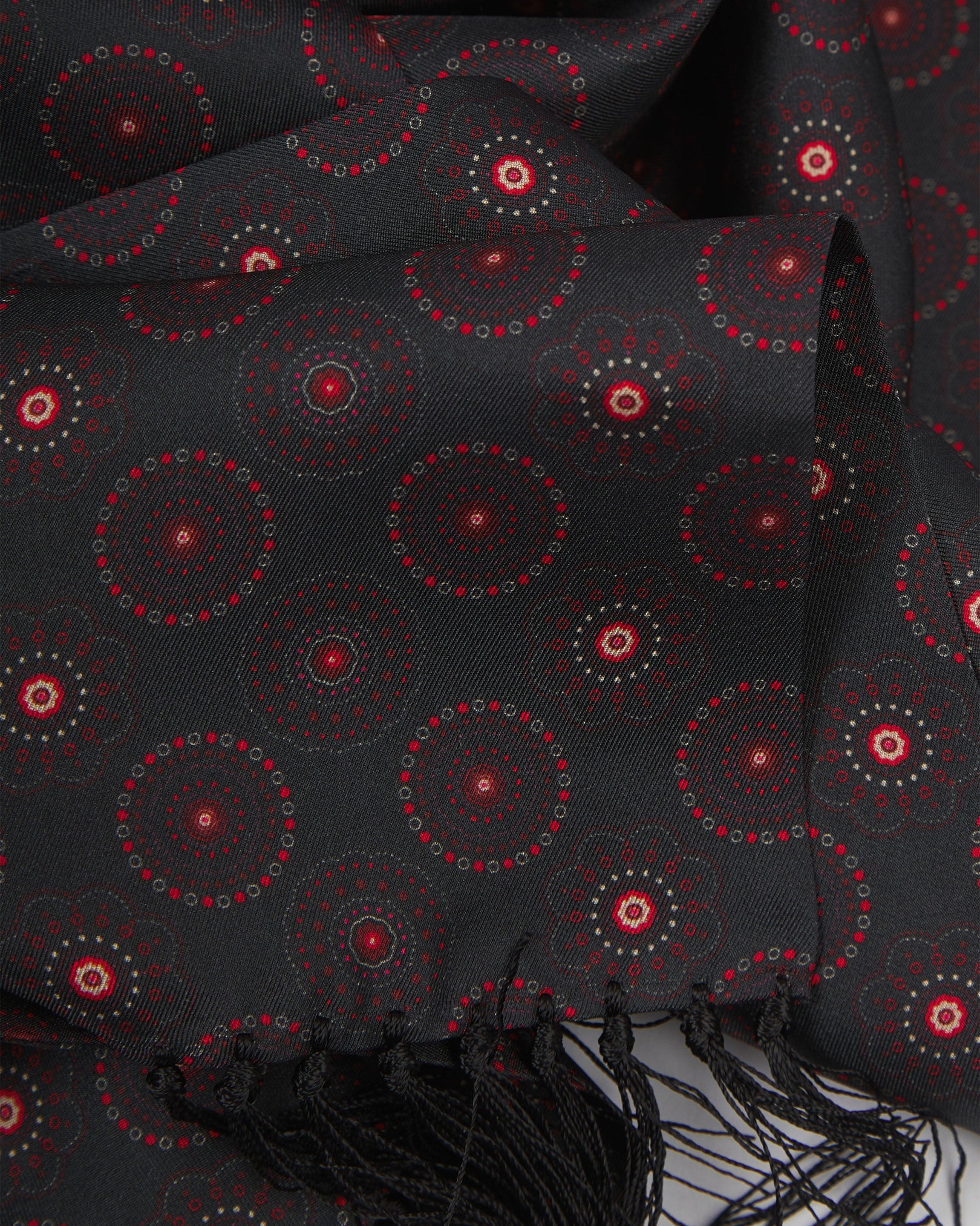 Ruffled close-up view of the Seattle Good Fortune silk aviator scarf, presenting a closer view of the red geometric circular patterns against a black background.