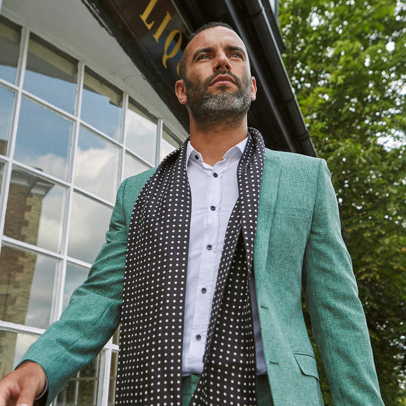 Outdoor walking pose of model wearing 'The Shinagawa' polka dot polyester scarf in black with white spots. Paired with a casual mint-green suit and white shirt.