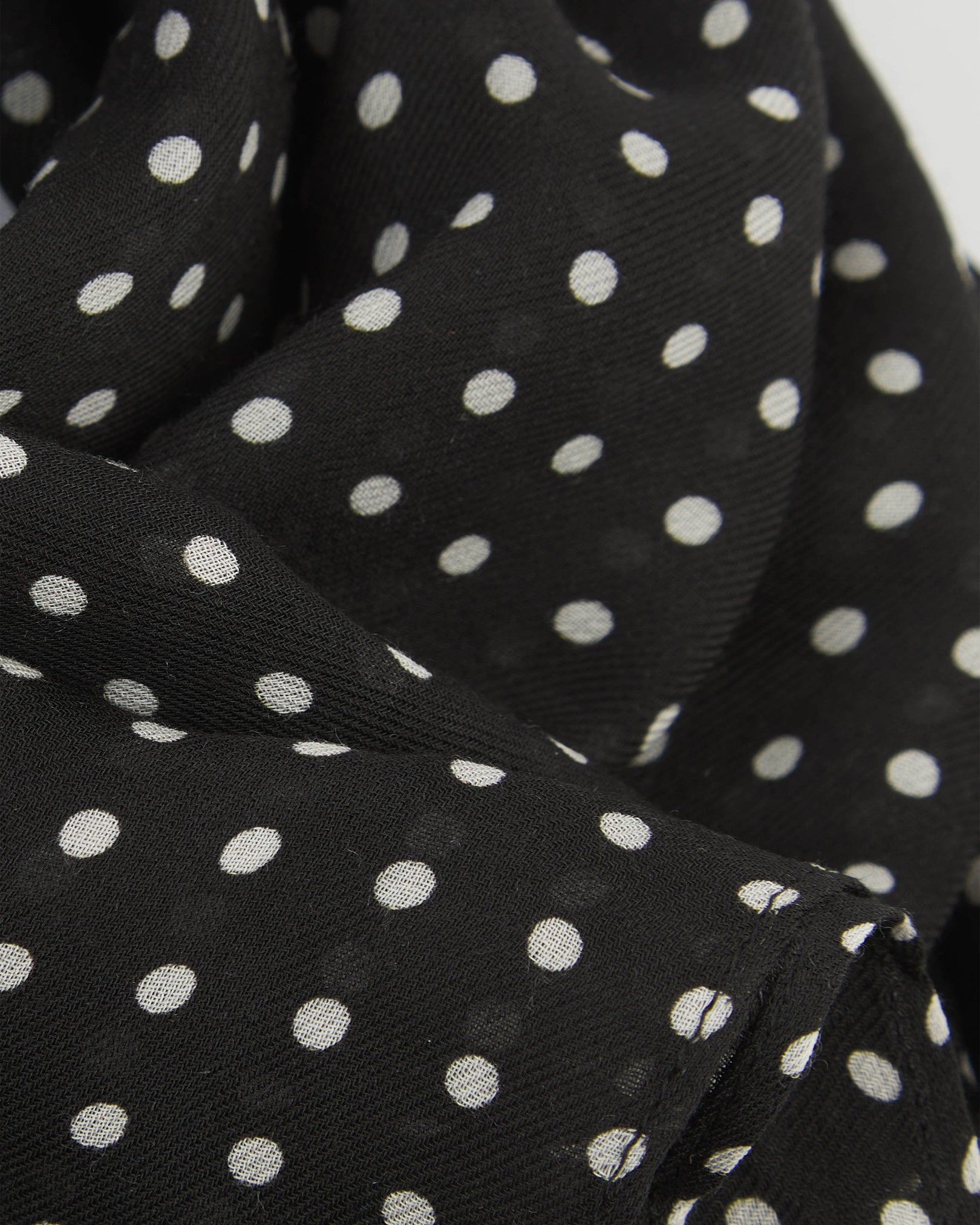 A ruffled close-up of The Shinagawa bohemian wide scarf, showing the soft modal and wool blend fabric with evenly spaced white polka dots on a black background.