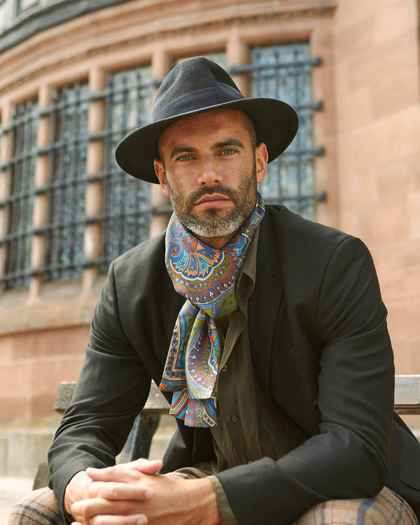 Close-up view of seated model wearing 'The Montreal' silk scarf snugly around neck in a simple knot and paired with a dark hat and jacket.
