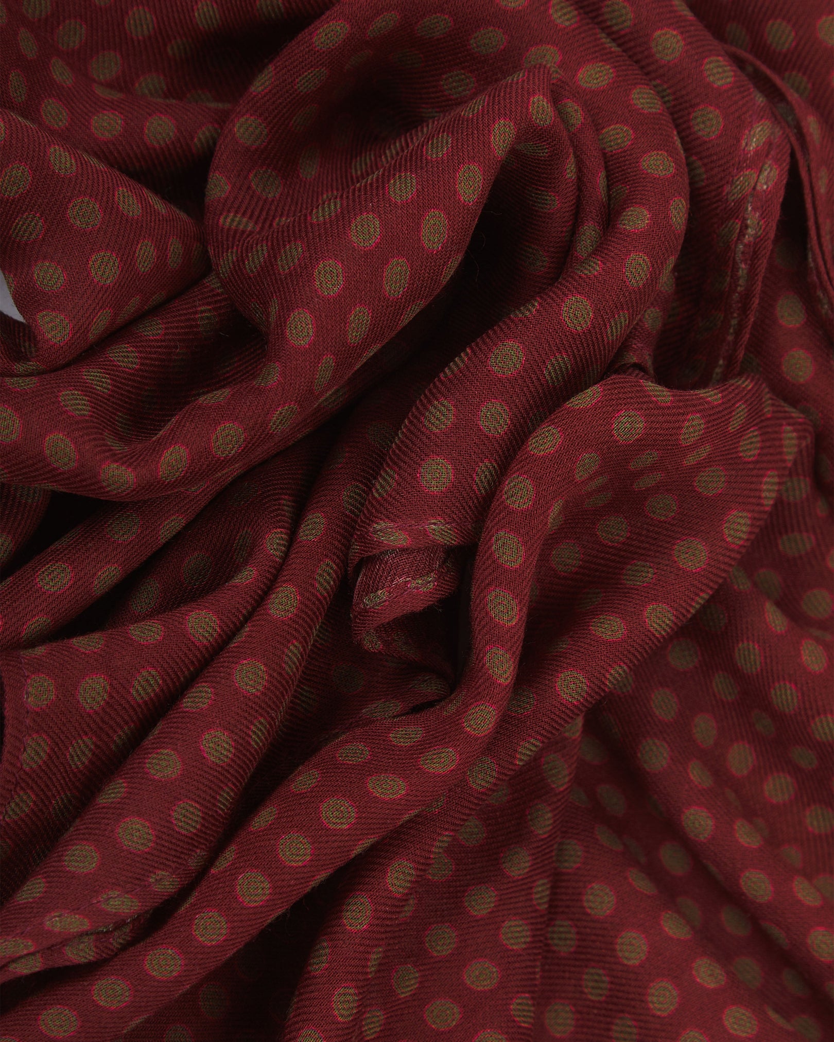 A ruffled close-up of the Skytree 'Good Fortune' bohemian wide scarf, showing the soft modal and wool blend fabric with neat rows of small concentric disc motifs in green and pink on a rich maroon background.