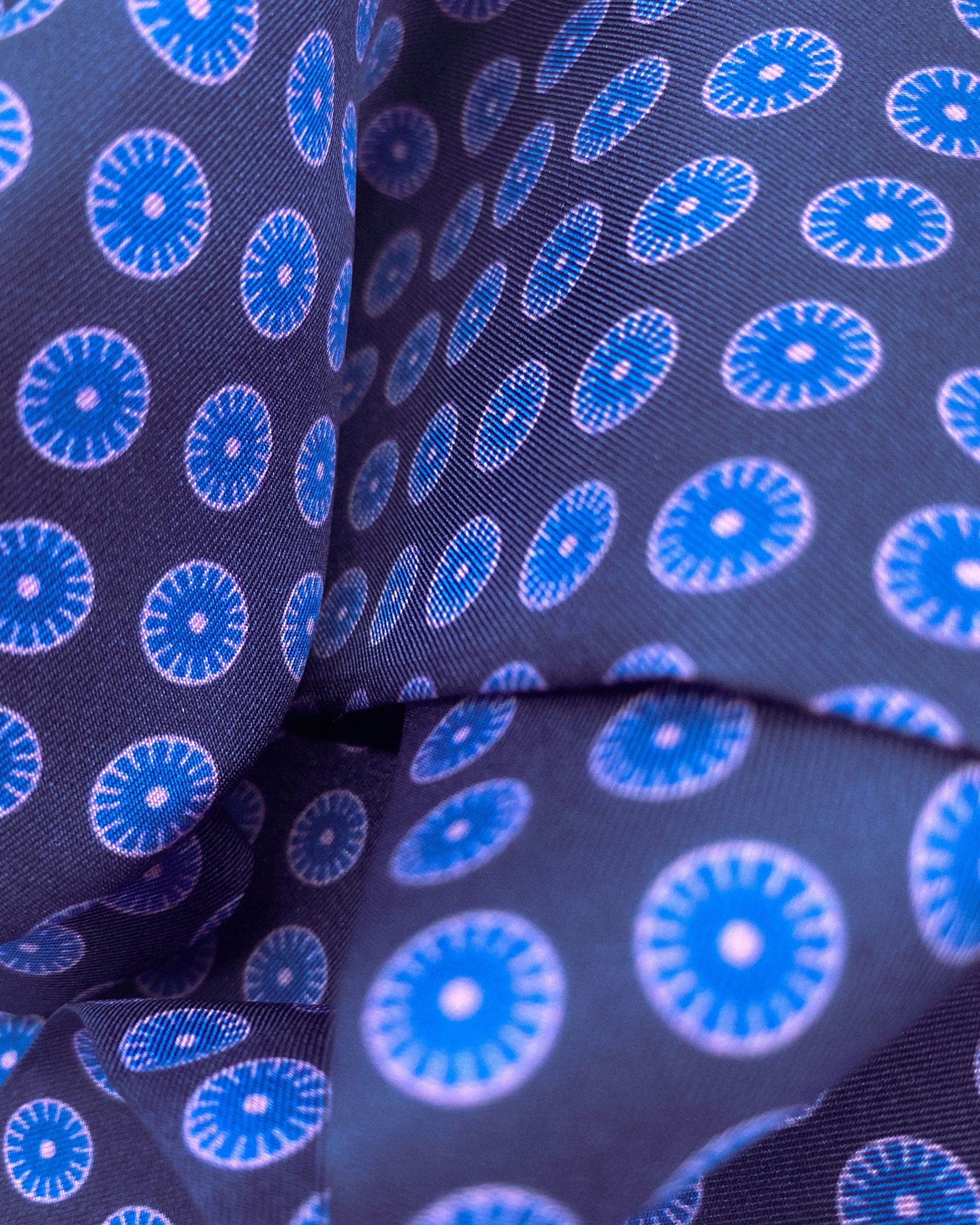 A ruffled close-up of the 'Skytree' silk scarf, presenting a closer view of the geometric small pale blue and pink discs against the deep blue background.