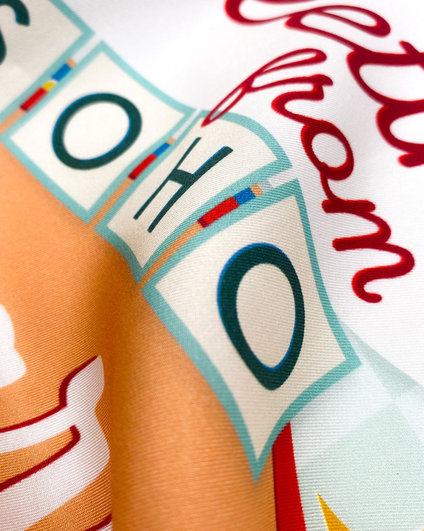A ruffled close-up of the 'Soho Sign' blue silk headscarf, presenting a closer look at a portion of the signage design and the material's subtle lustre.