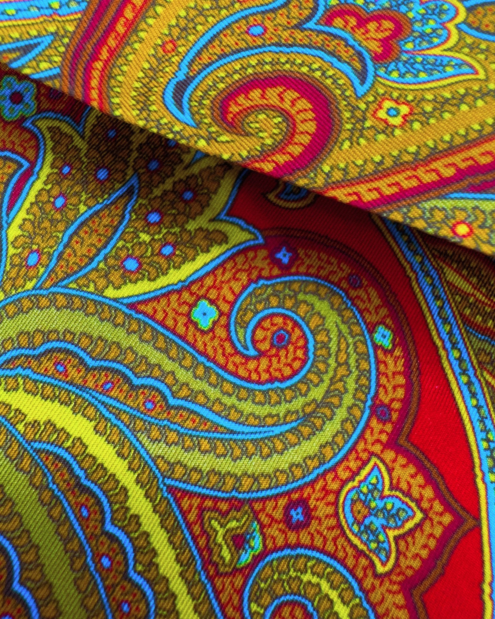 A close-up, ruffled view of 'The Victoria' multicoloured paisley polyester scarf on a rich, red background. Clearly showing the blue, gold and pink paisley patterns.