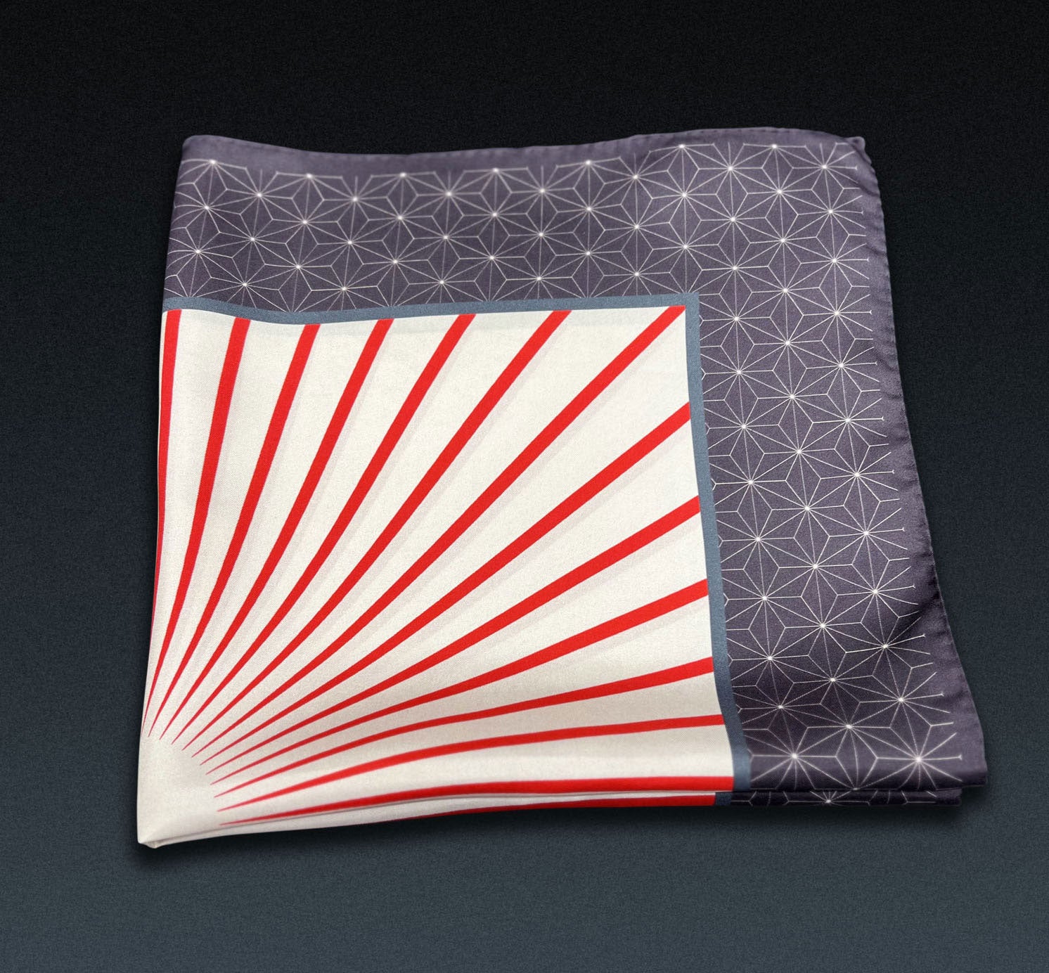 Red starburst 'Sun' neckerchief folded into a quarter, showing red, linear pattern and grey border.