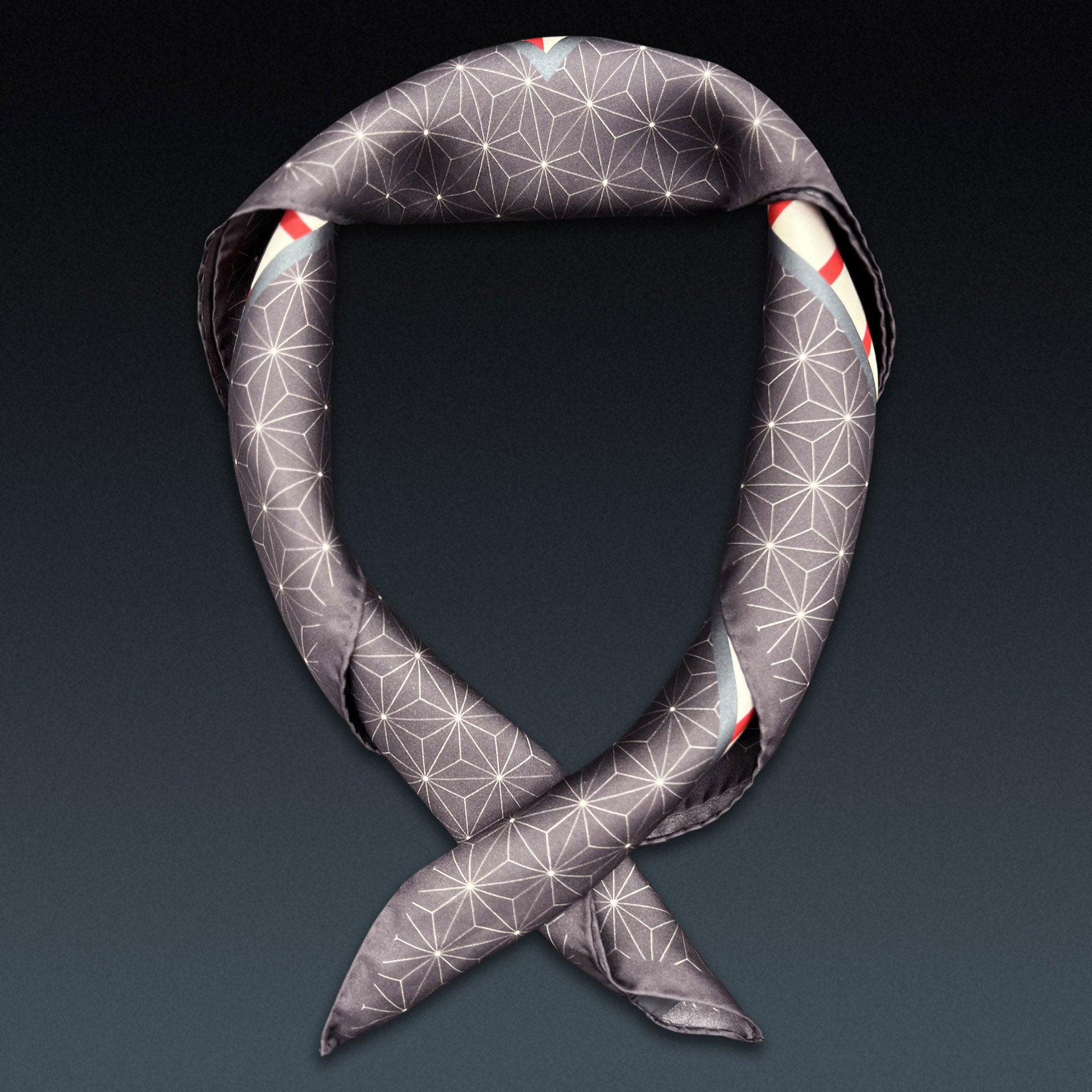 Red starburst 'Sun' neckerchief twisted and curled into a loop on a dark background.