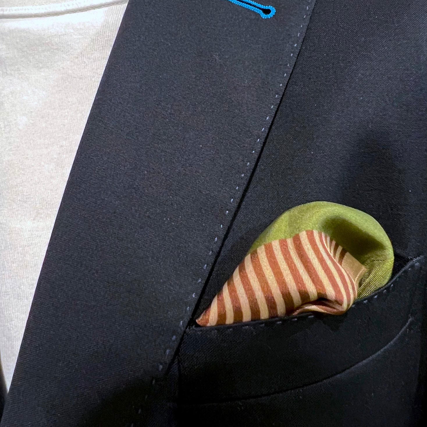 Silk square handkerchief with retro-inspired pattern on a sapphire-green background and placed in a jacket breast pocket.