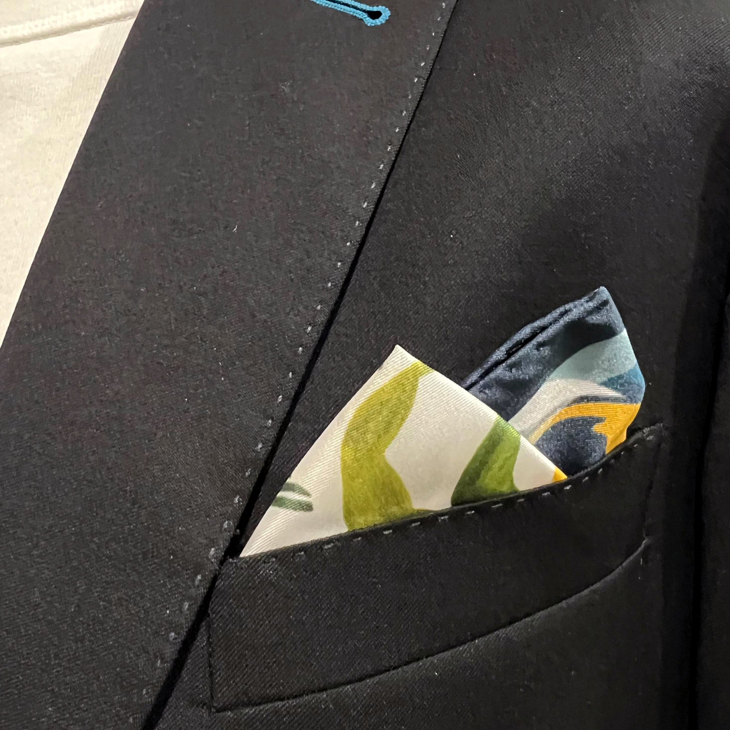 Silk square handkerchief with toucan bird pattern on a blue ground and placed in a jacket breast pocket.