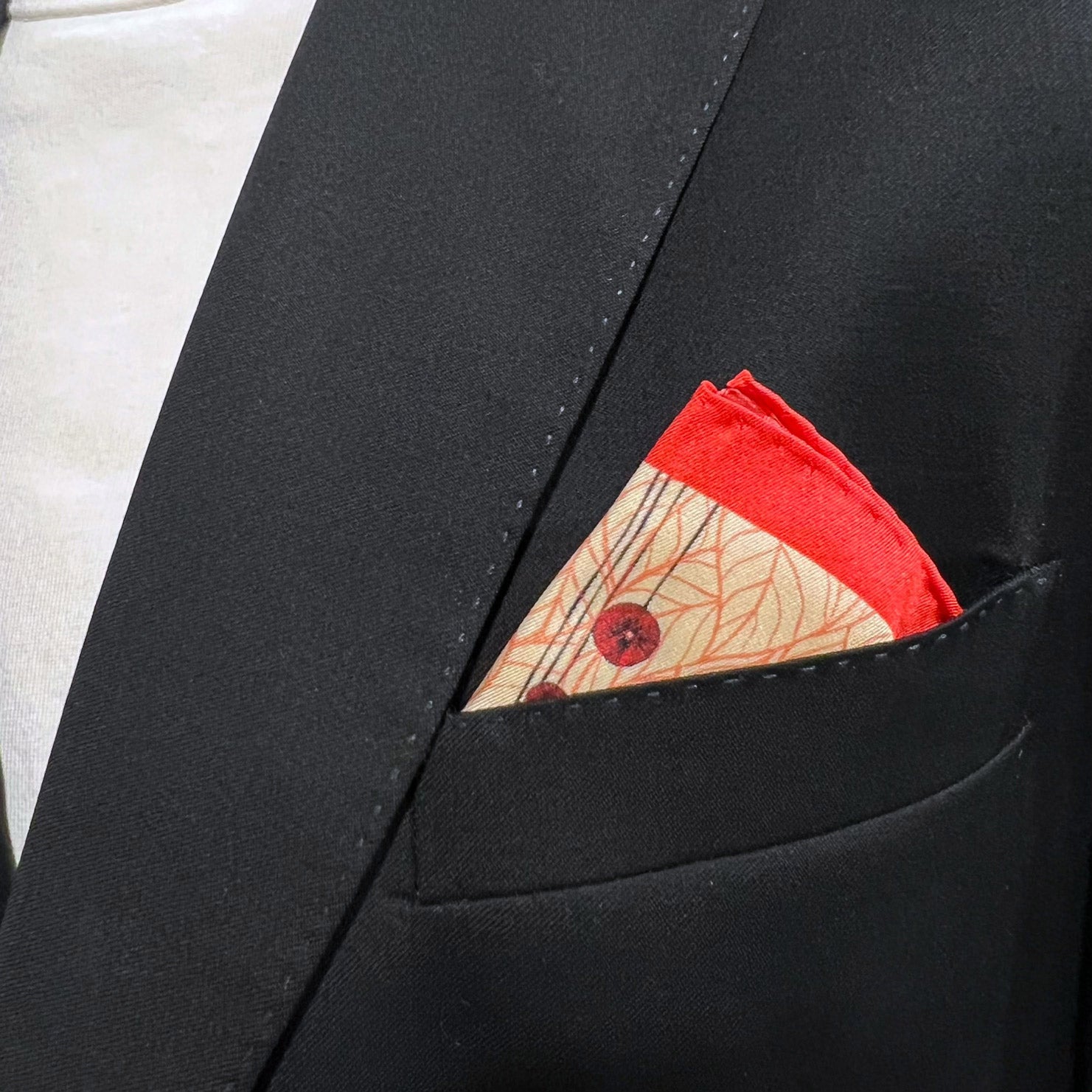 Silk square handkerchief with stylised red poppy flowers motif. Placed in a jacket breast pocket.