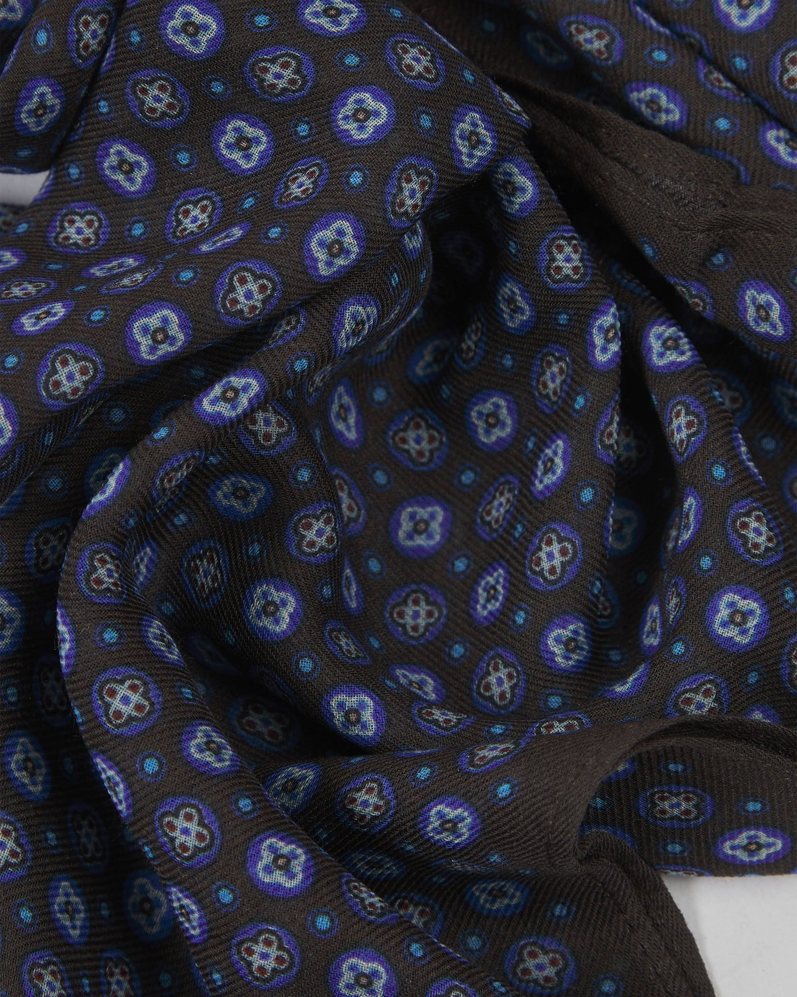 A ruffled close-up of the Toshima 'Mahogany Daze' bohemian wide scarf, showing the soft modal and wool blend fabric with small stylised floral motifs in purple and blue on a rich mahogany brown background.