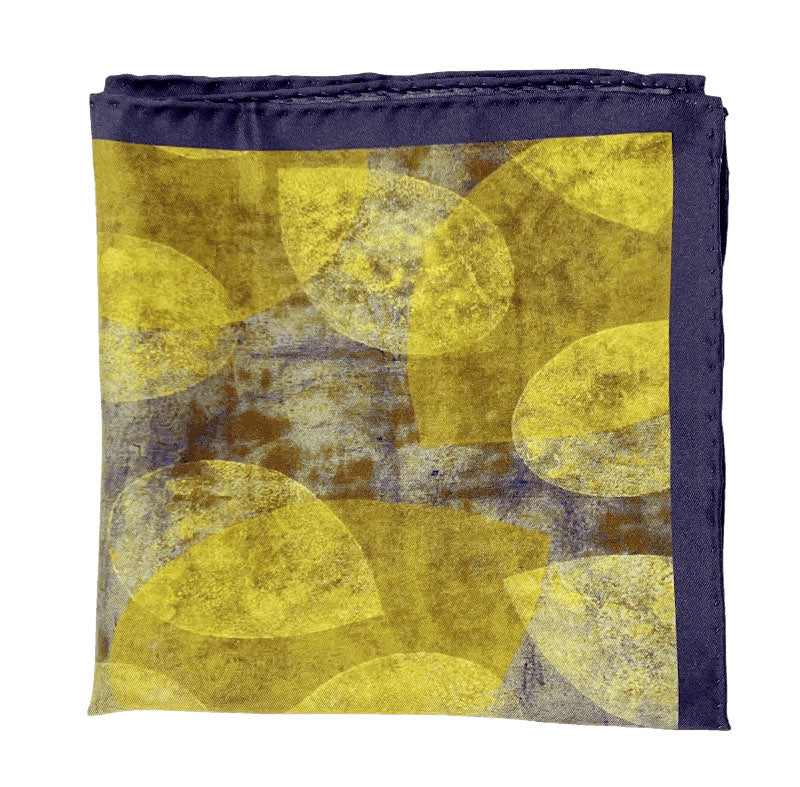 The 'Tweed' silk pocket square from SOHO Scarves folded into a quarter, showing the stylised leaf forms creating a yellow and purple textured effect.