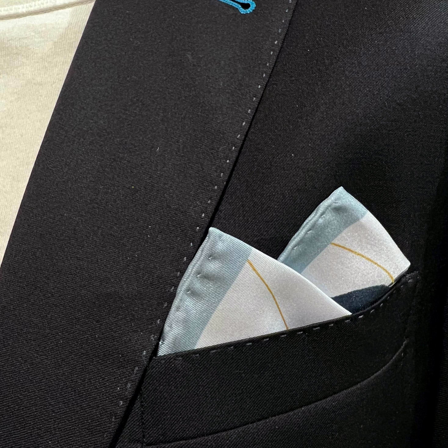 Silk square handkerchief with blue leaf pattern and placed in a jacket breast pocket.