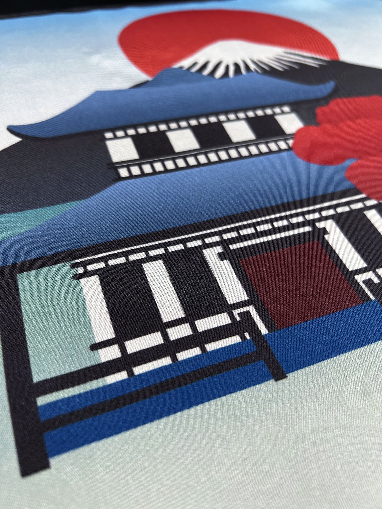 Angled close-up of the 'House' pocket square in pure silk. Focus on the Japanese style building with rising sun and Mount Fuji background.