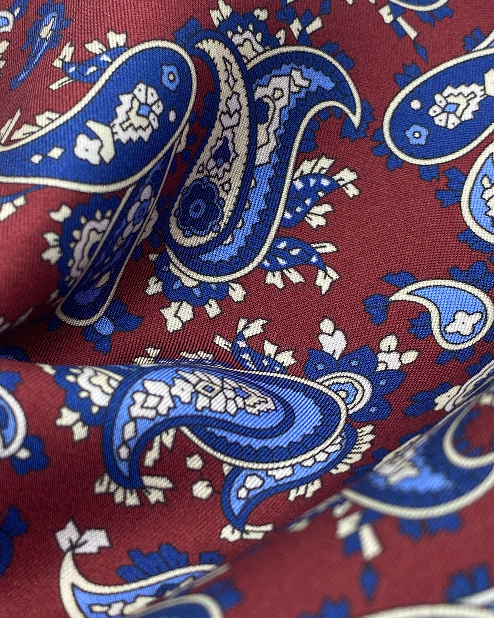 A ruffled close-up of the burgundy and blue patterned 100 percent silk scarf, presenting a closer view of the royal-blue and cream paisley patterns.