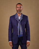 Portrait view of male model wearing 'The Auburn' silk aviator scarf. Tied loosely around neck in a simple knot and shoulders and paired with a smart, midnight-blue suit.