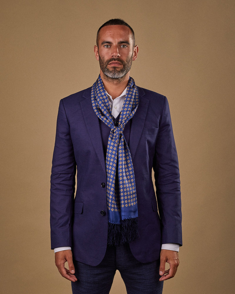 Portrait view of male model wearing 'The Auburn' silk aviator scarf. Tied loosely around neck in a simple knot and shoulders and paired with a smart, midnight-blue suit.
