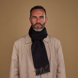 Man wearing Soho Scarves' black cashmere scarf in a classic knot. Paired with fawn three-quarter length coat.