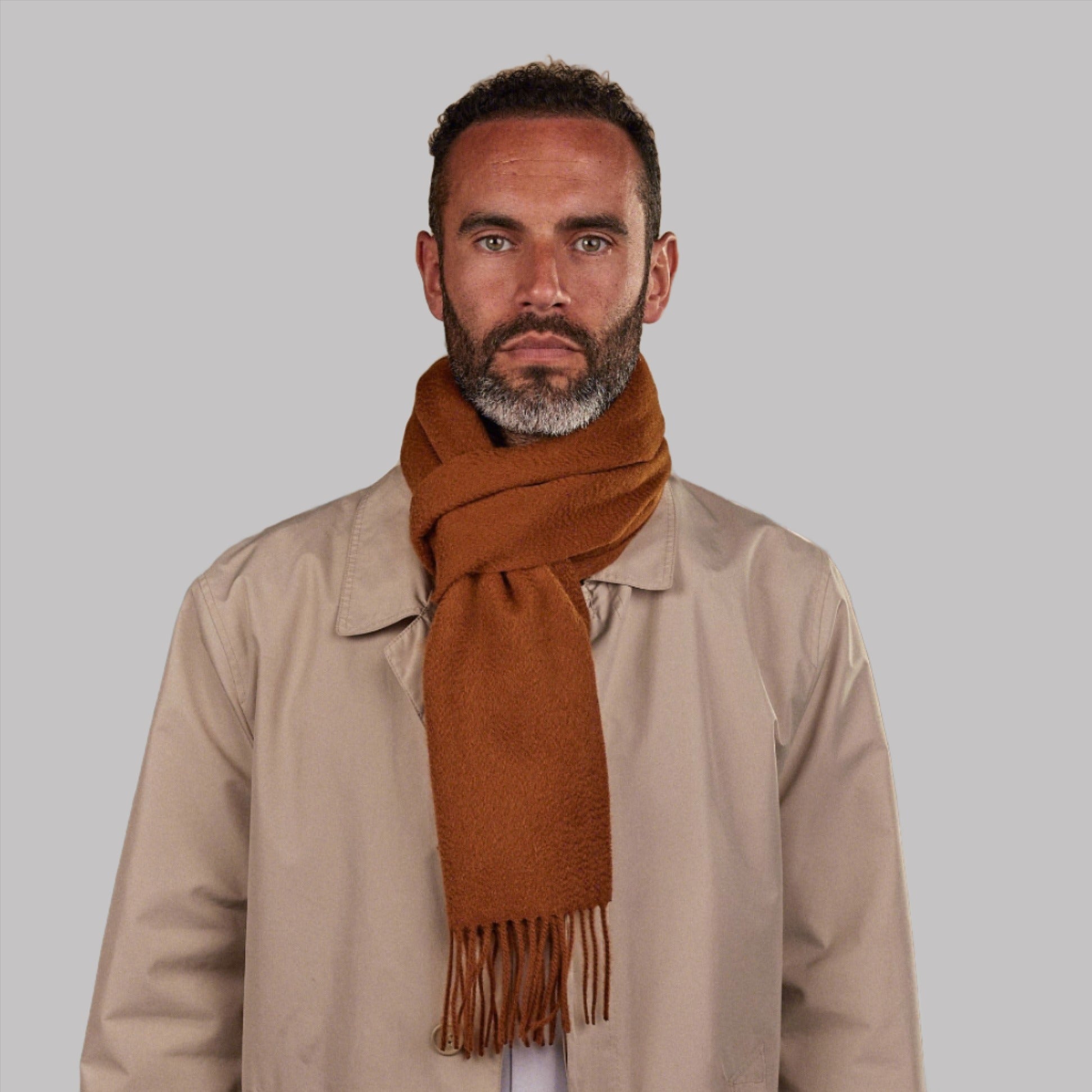 Man wearing Soho Scarves' orange-brown cashmere scarf in a classic knot. Paired with fawn three-quarter length coat.
