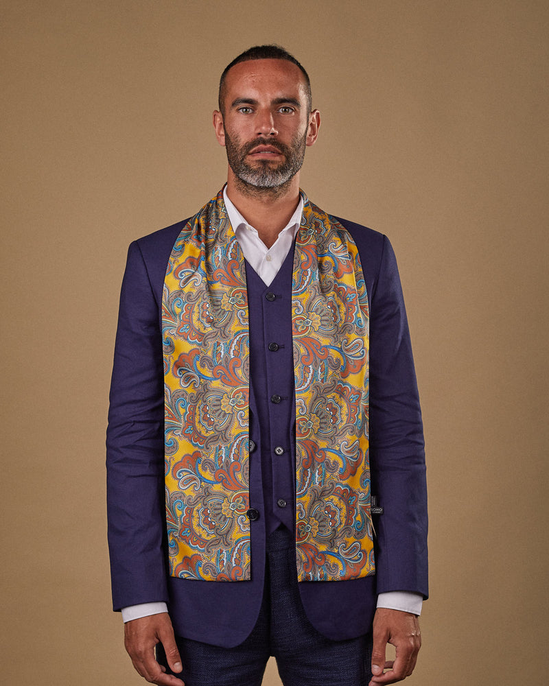 Portrait view of male model looking straight ahead, wearing 'The Carnaby' polyester scarf. Draped loosely around shoulders and neck and paired with a smart, midnight-blue suit.