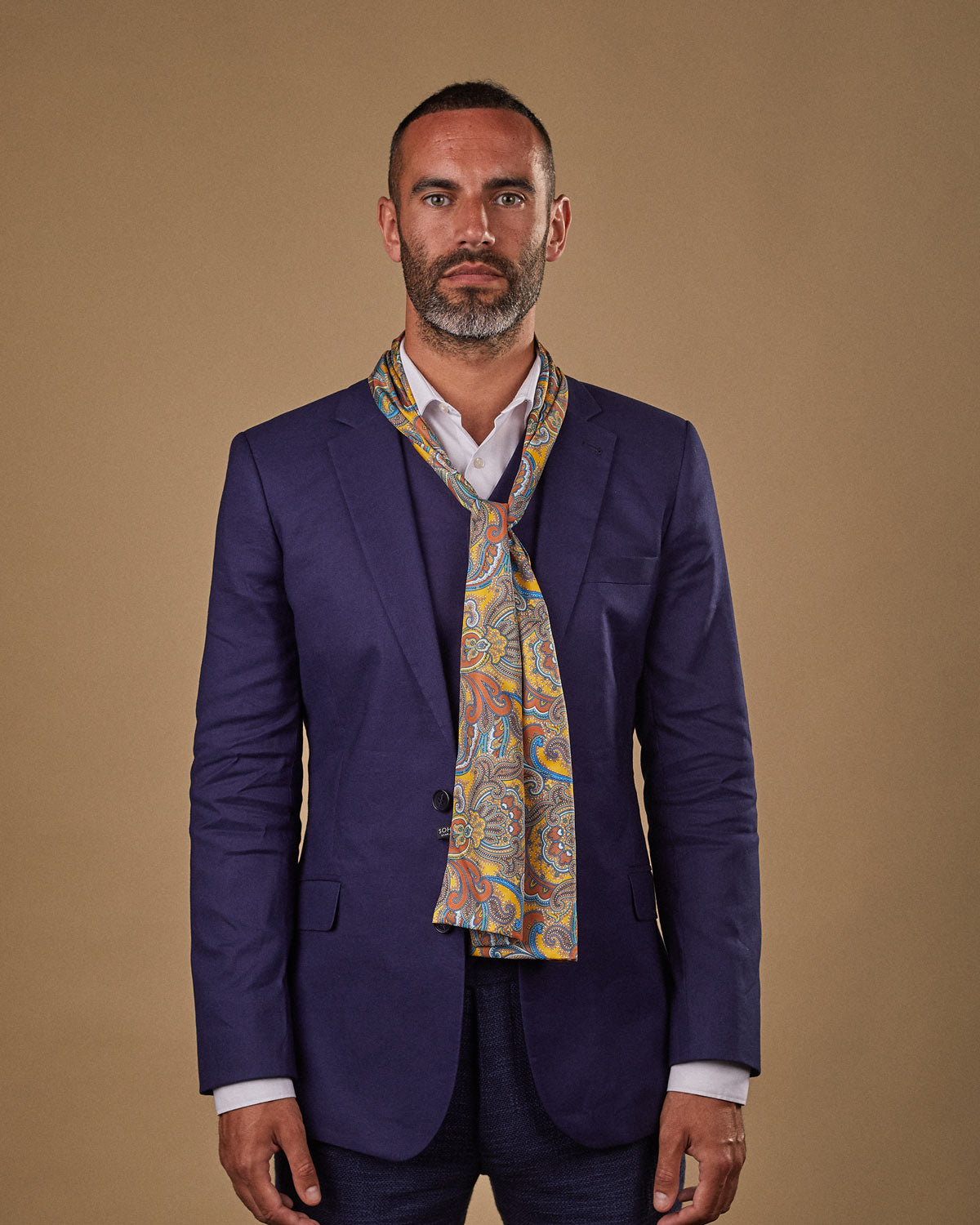 Portrait view of male model wearing 'The Carnaby' silk scarf. Tied loosely around neck in a simple knot and shoulders and paired with a smart, midnight-blue suit.
