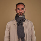 Man wearing Soho Scarves' charcoal-grey cashmere scarf in a classic knot. Paired with fawn three-quarter length coat.