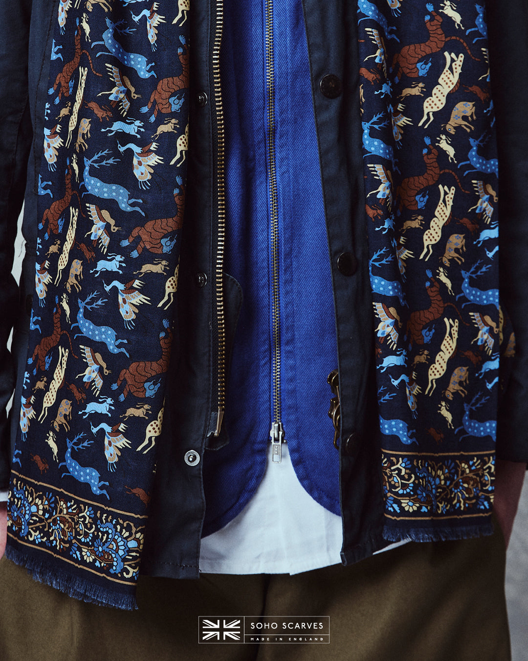 Close-up of man wearing the English-made, 'Woodland Creatures in Airforce Blue' silk and wool scarf, with focus on the blue and brown woodland creature motifs and floral border.